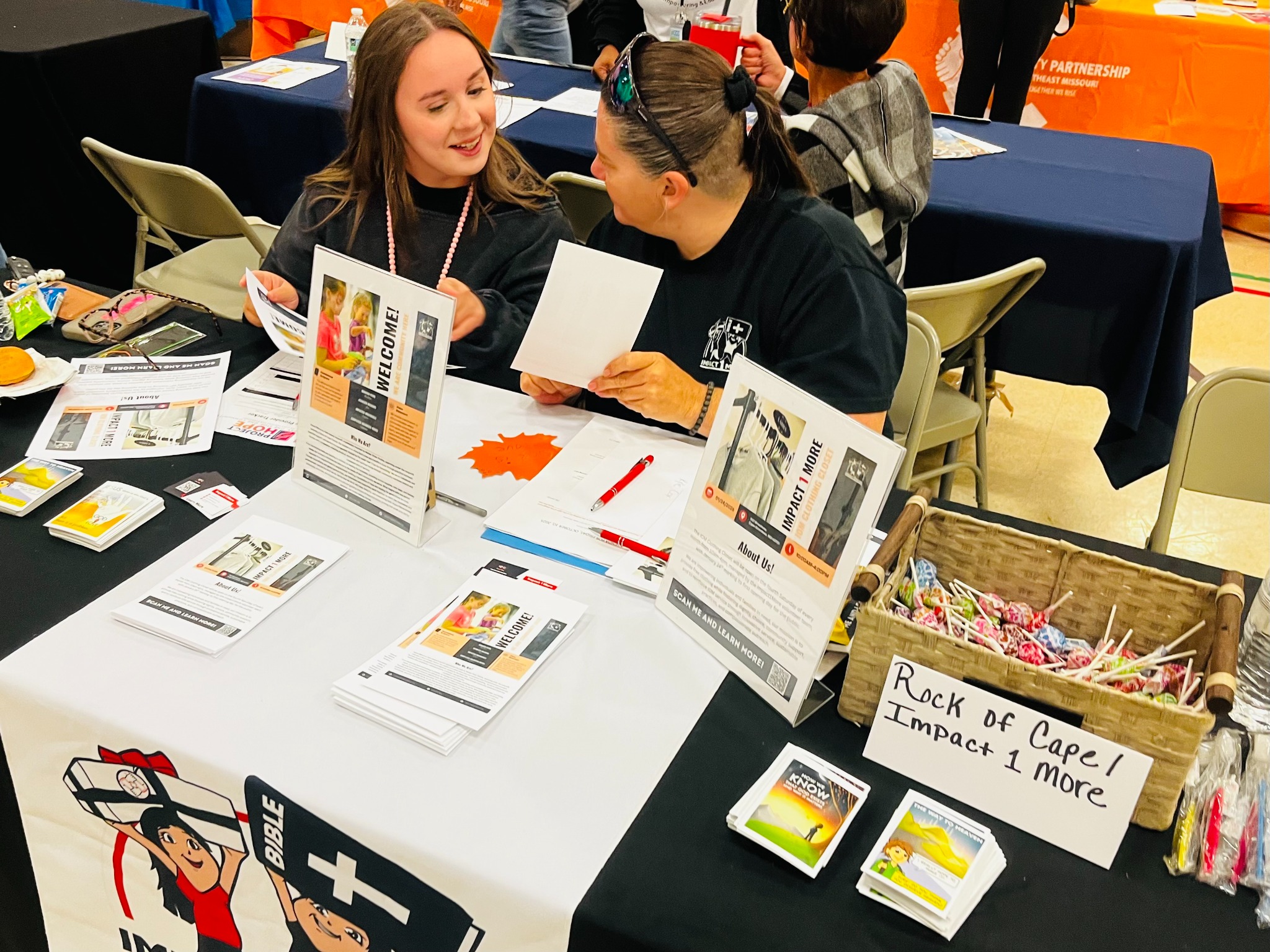 Impact One More volunteers communicating at a community outreach table